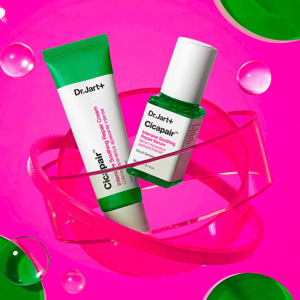 Dr.Jart+ Cicapair Intensive Soothing Repair Cream a Serum v zelených obaloch, ktoré stoja na ružovej kruhovej základni. Produkty sú vyvinuté na upokojenie a opravu podráždenej pokožky.