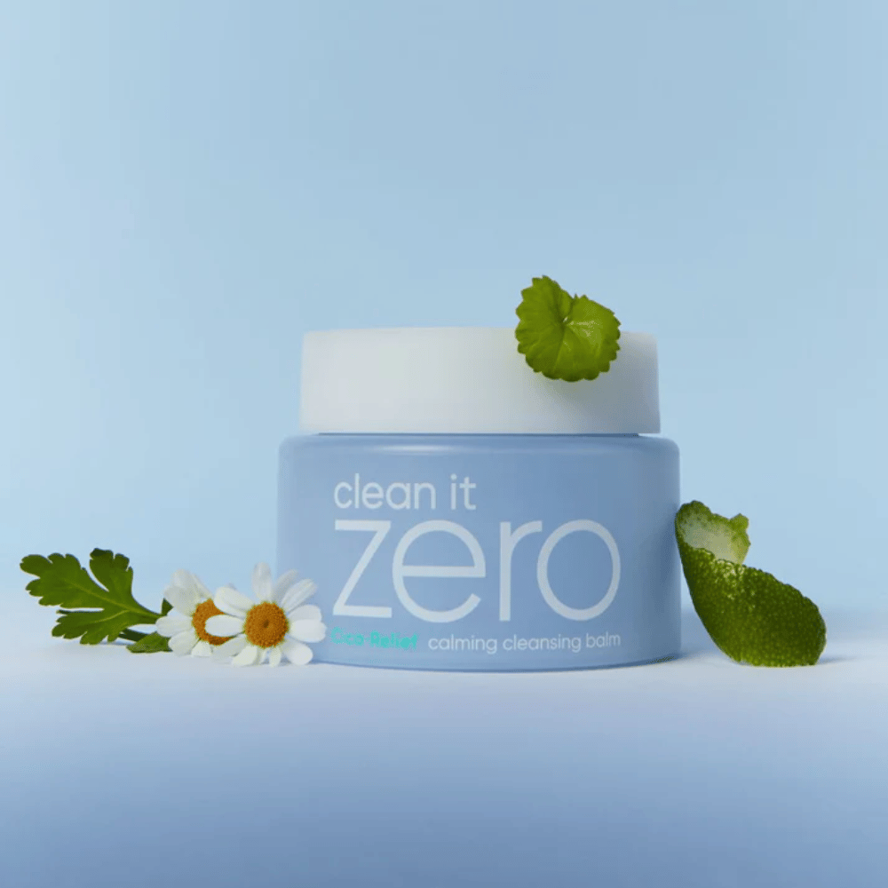 Clean It Zero Cica-Relief Calming Cleansing Balm umiestnený s rastlinami a kvetmi, ilustruje jemné čistenie s upokojujúcou CICA pre citlivú a podráždenú pokožku.
