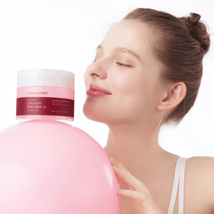 Žena stojí s ružovou loptou a pohárom Collagen Pore-Tight Up Gel Toner Pads, zatiaľ čo sa usmieva a drží pohár blízko svojej tváre. Pohár je označený názvom produktu a obsahuje tonerové podložky, ktoré pomáhajú spevniť pokožku a zmenšiť veľkosť pórov.