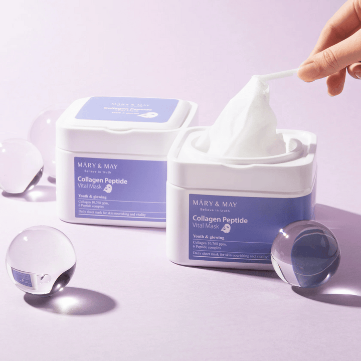 Ruka vyberá masku z nádoby s MARY & MAY Collagen Peptide Vital Mask. Maska je určená na každodenné použitie na výživu a žiaru pokožky, s kolagénom a peptidmi na podporu mladistvosti pokožky.