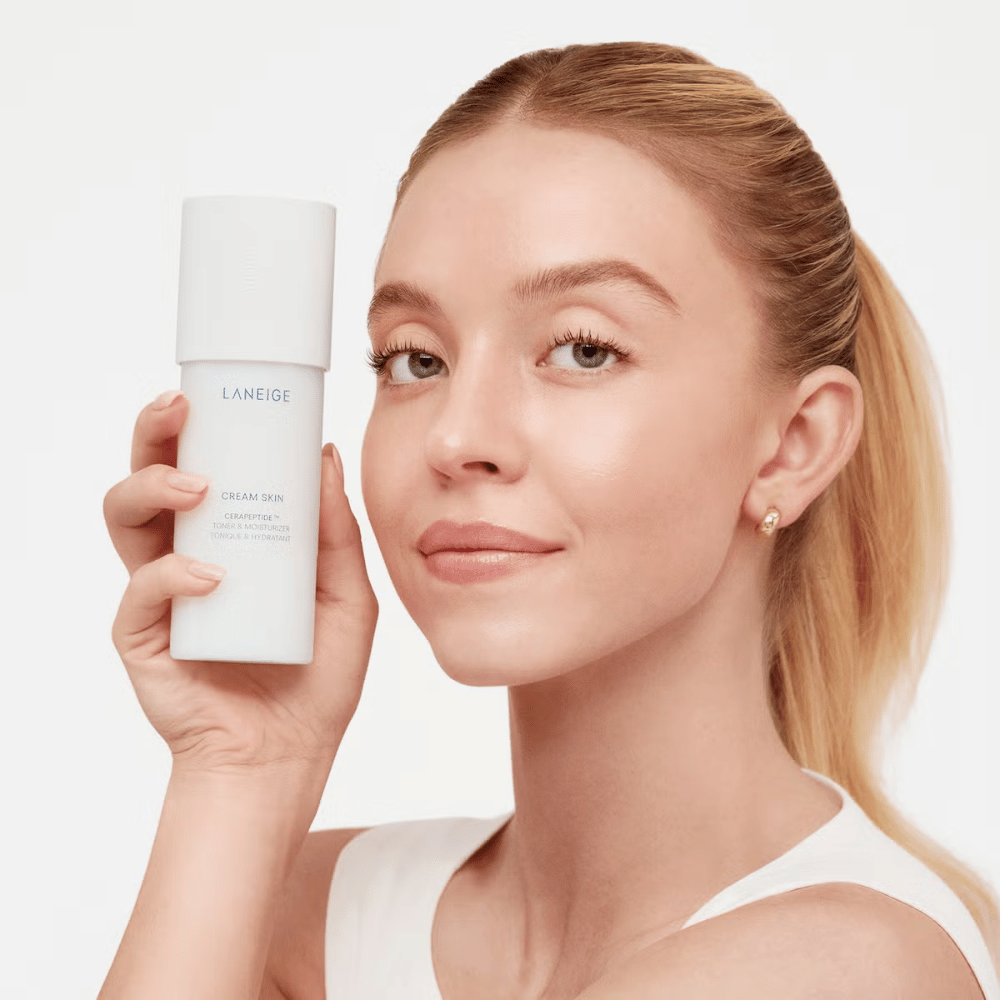 Osoba drží Laneige Cream Skin Cerapeptide Refiner v bielej fľaši. Osoba sa usmieva a ukazuje produkt, ktorý sa propaguje ako hydratačný toner a produkt starostlivosti o pleť.