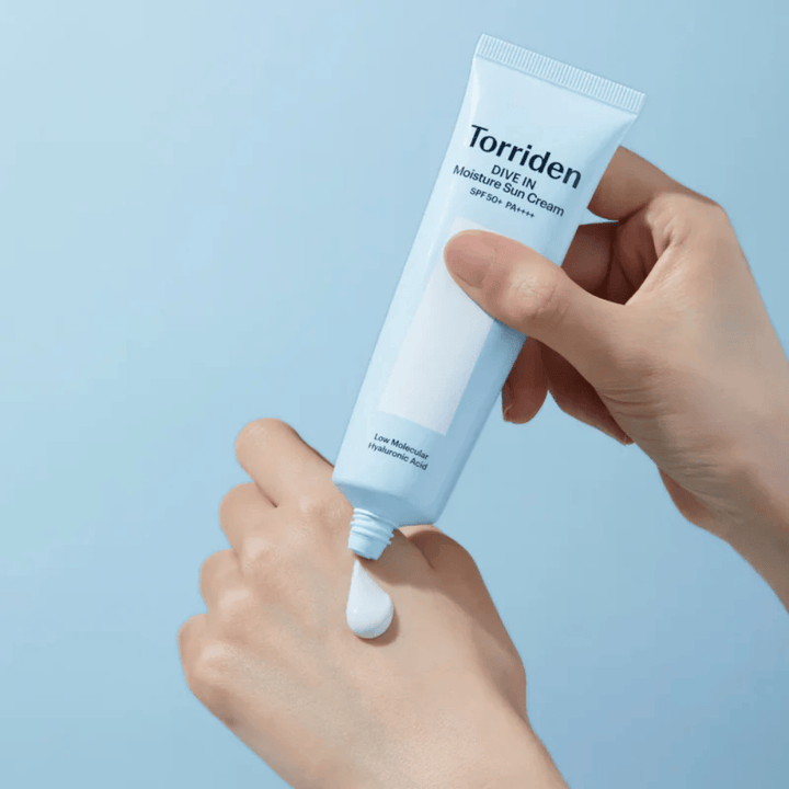 Torriden DIVE-IN Moisture Sun Cream SPF50+ PA++++ sa nanáša na ruku, aby ukázal ľahkú a krémovú konzistenciu hydratačného opaľovacieho krému.