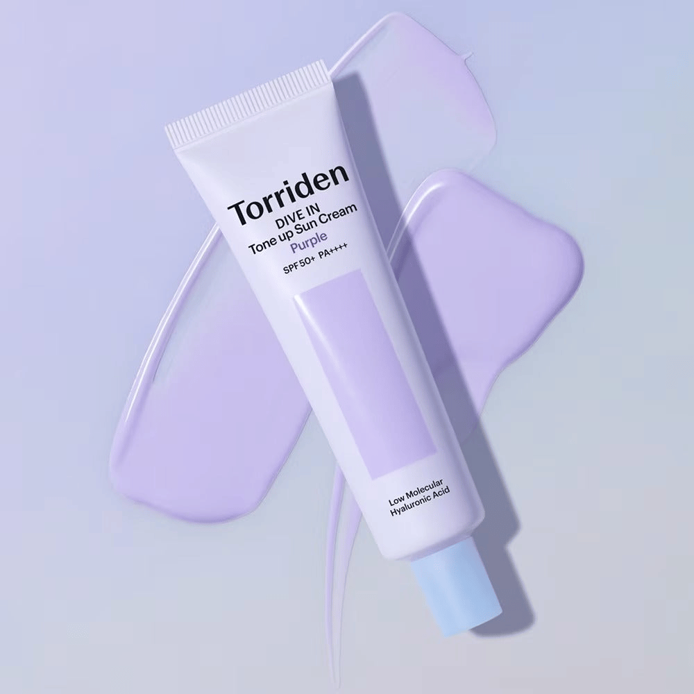 Torriden DIVE IN Tone Up Sun Cream Purple umiestnený na rozotretom fialovom kréme, ktorý zvýrazňuje efekt zjednotenia tónu pleti a rozjasnenia.