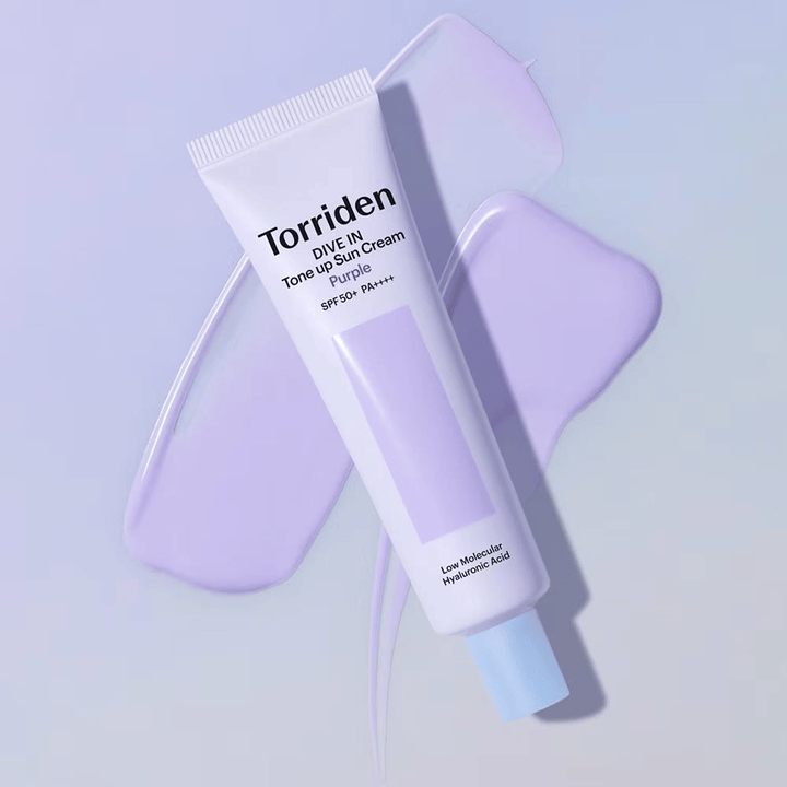 Torriden DIVE IN Tone Up Sun Cream Purple umiestnený na rozotretom fialovom kréme, ktorý zvýrazňuje efekt zjednotenia tónu pleti a rozjasnenia.