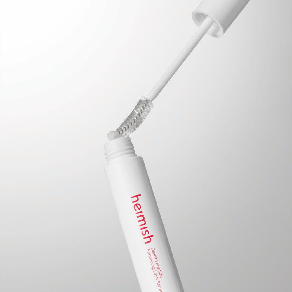 Detailný záber na aplikátor Heimish Dailism Peptide Enhancing Lash Serum. Kefka sa vyťahuje z bielej nádobky a ukazuje transparentné sérum, ktoré sa aplikuje na riasy.