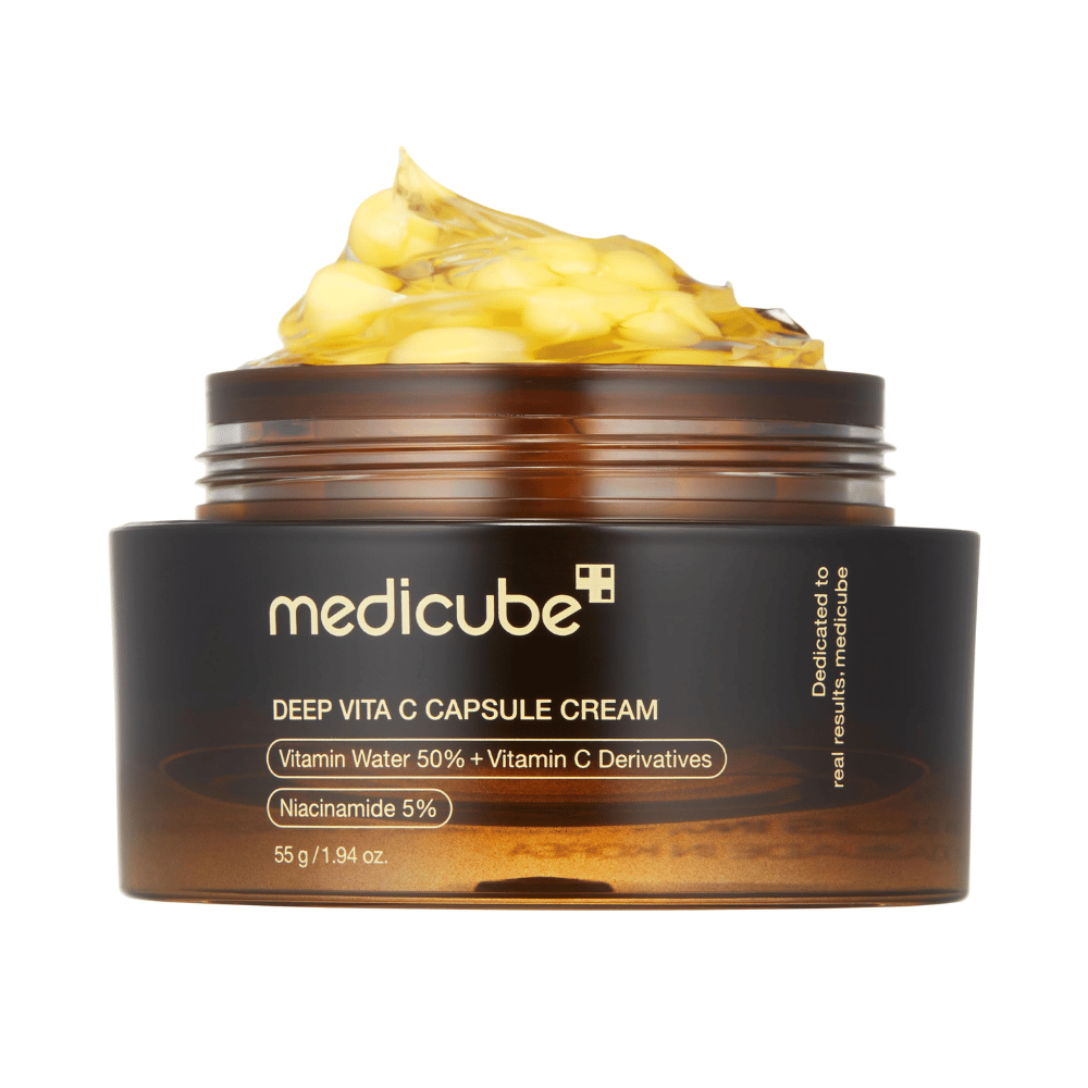 Detailný záber na "Medicube Deep Vita C Capsule Cream," ktorý ukazuje konzistenciu krému a kapsuly vitamínu C. Balenie je tmavohnedé so zlatým textom a opisuje obsah vitamínovej vody (50 %) a niacínamidu (5 %), čo poskytuje vizuálnu prezentáciu hydratačných a zlepšujúcich vlastností produktu.