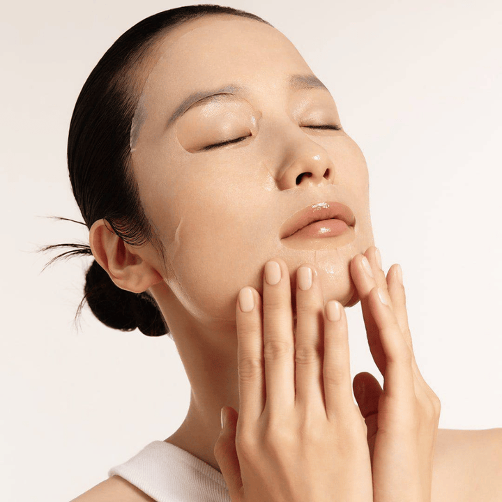 Model s hydratovanou a žiarivou pokožkou aplikuje sheet masku, zameranie na žiarivosť, hladký tón pleti a lesk.