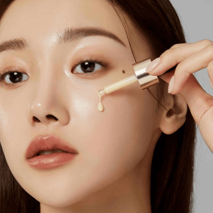 Detailný záber na ženu, ktorá aplikuje Medicube Deep Vita C Ampoule so zlatou pipetou. Kvapka séra je na ceste k jej pokožke, ktorá má prirodzený lesk. Perfektné na dosiahnutie svetlejšieho a rovnomernejšieho tónu pleti.