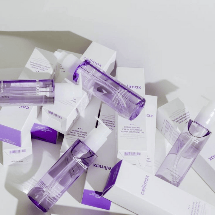 Celimax Derma Nature Fresh Blackhead Jojoba Cleansing Oil vo fialových fľašiach umiestnené medzi bielymi obalmi produktov s fialovými detailmi.