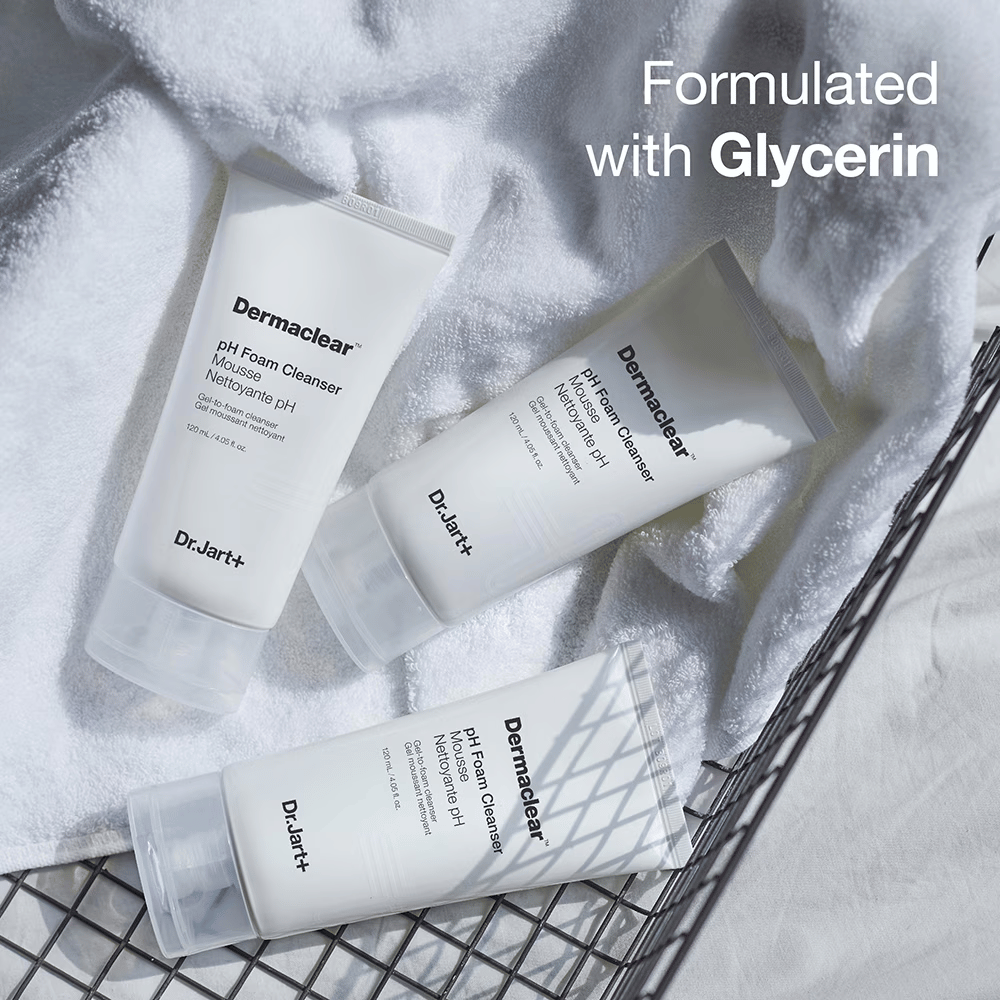 Tri tuby Dr.Jart+ Dermaclear pH Foam Cleanser ležia na bielej froté uteráku v kovovom koši, s textom "Formulované s glycerínom" v hornom rohu.
