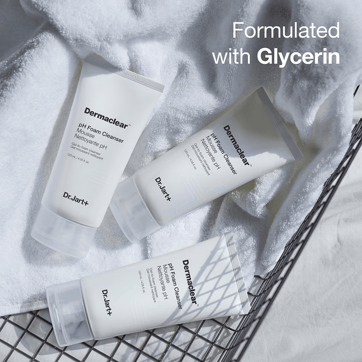 Tri tuby Dr.Jart+ Dermaclear pH Foam Cleanser ležia na bielej froté uteráku v kovovom koši, s textom "Formulované s glycerínom" v hornom rohu.