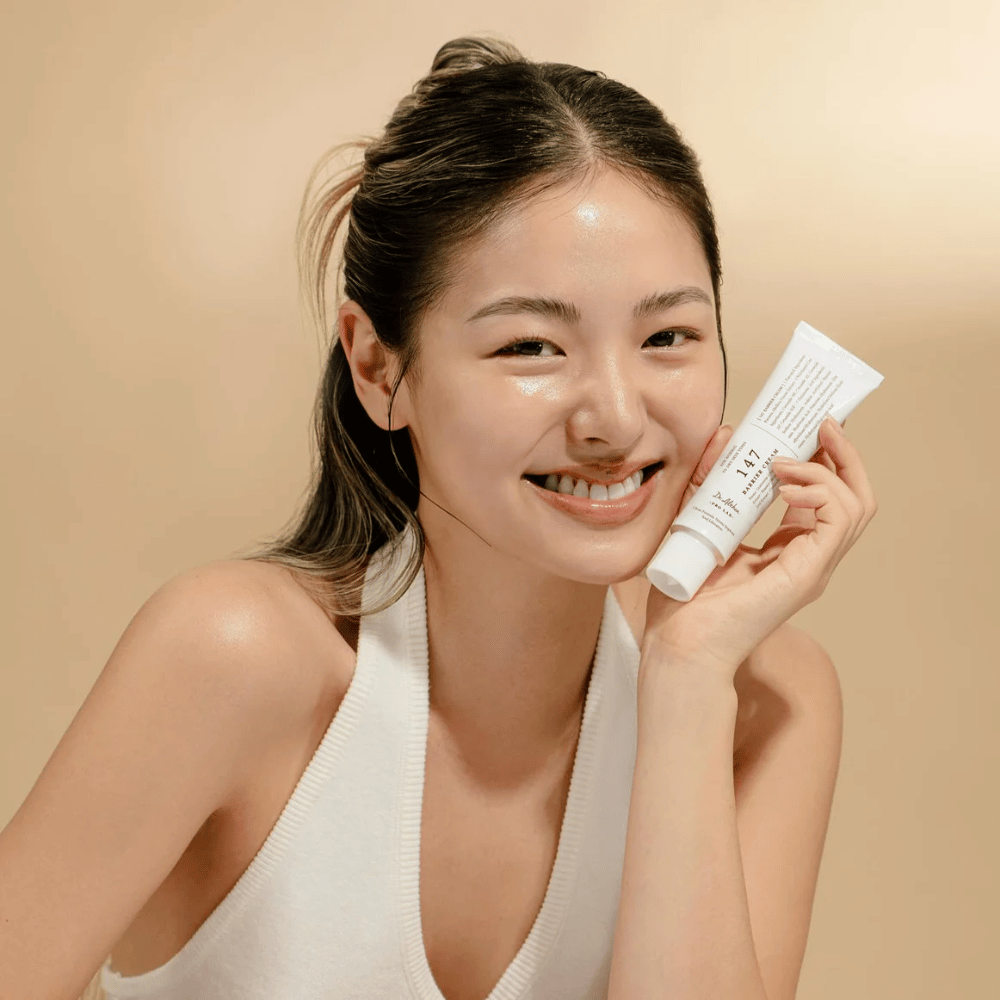 Modelka so žiarivou pleťou, ktorá sa usmieva a drží Dr. Althea 147 Barrier Cream – kórejský pleťový krém na kožnú bariéru a hydratáciu.