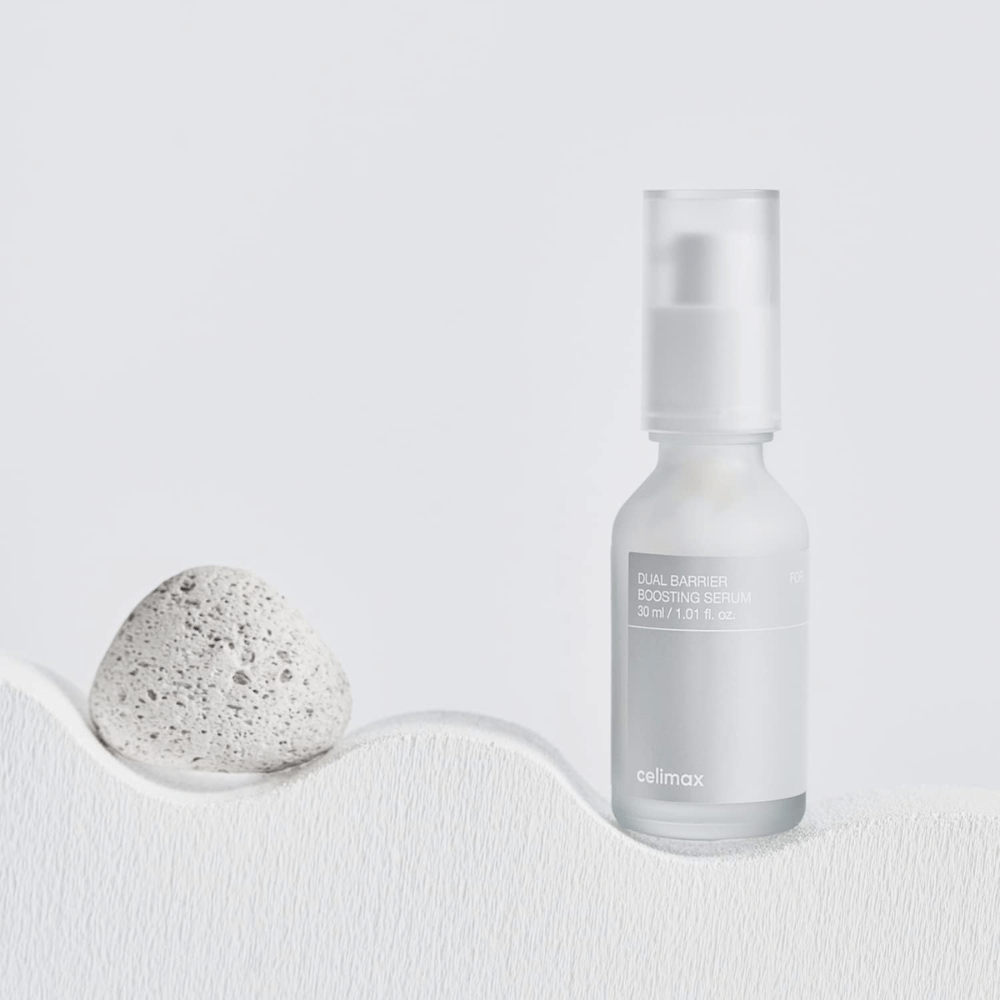 Celimax Dual Barrier Boosting Serum umiestnené na textílii s kameňom, pokojný produktový obrázok signalizujúci hydratáciu a posilnenú kožnú bariéru.