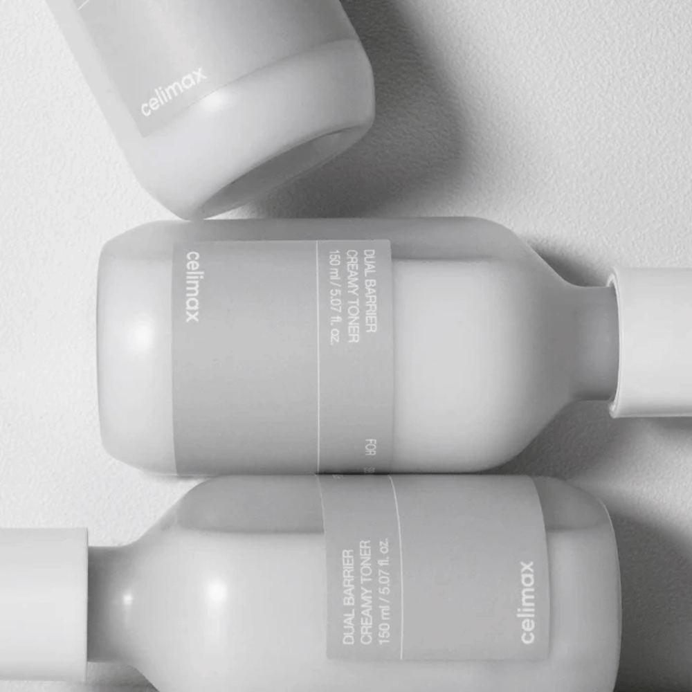 Tri ležiace fľaše Celimax Dual Barrier Creamy Toner v minimalistickom dizajne so sivou etiketou a jemným svetlom – ideálne pre citlivú a suchú pokožku.