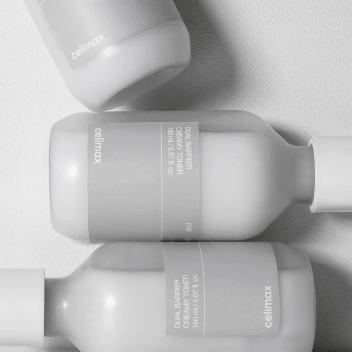 Tri ležiace fľaše Celimax Dual Barrier Creamy Toner v minimalistickom dizajne so sivou etiketou a jemným svetlom – ideálne pre citlivú a suchú pokožku.