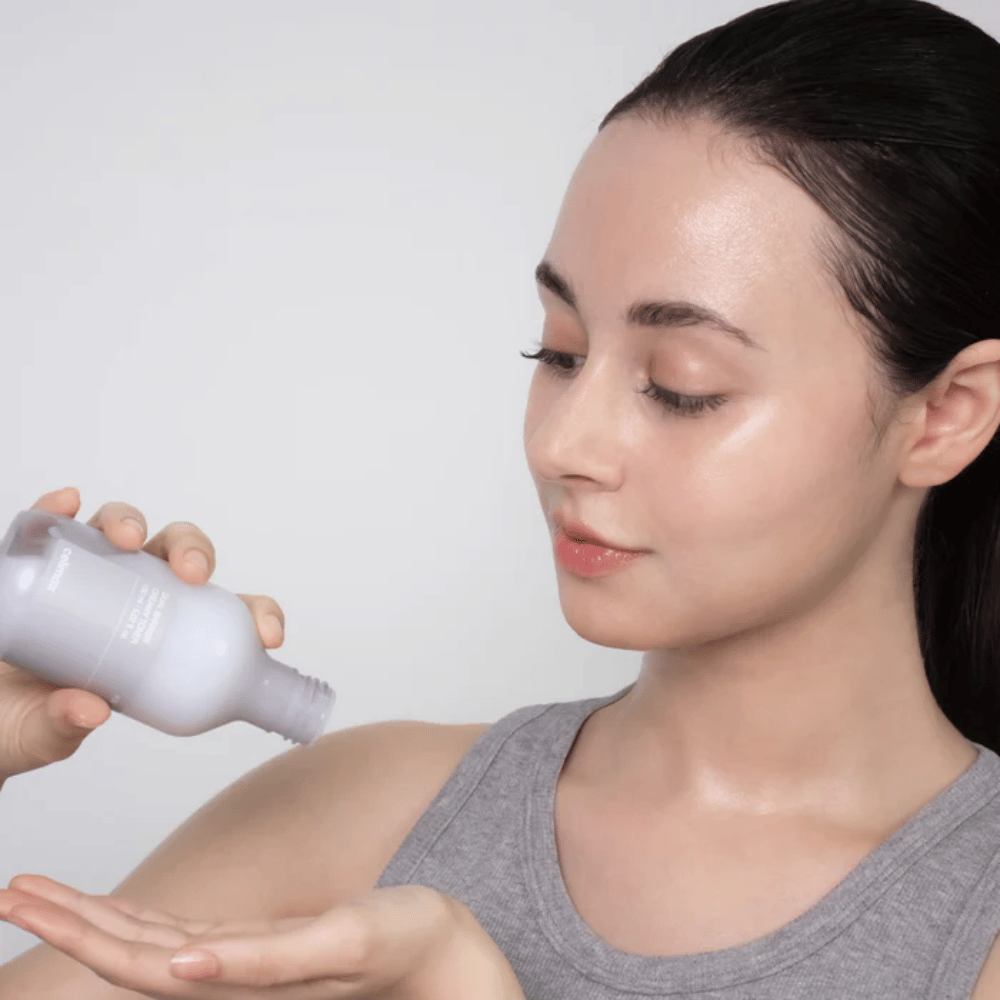 Žena s lesklou, hydratovanou pokožkou aplikuje Celimax Dual Barrier Creamy Toner tým, že naleje produkt do dlane pred svojou starostlivosťou o pleť.
