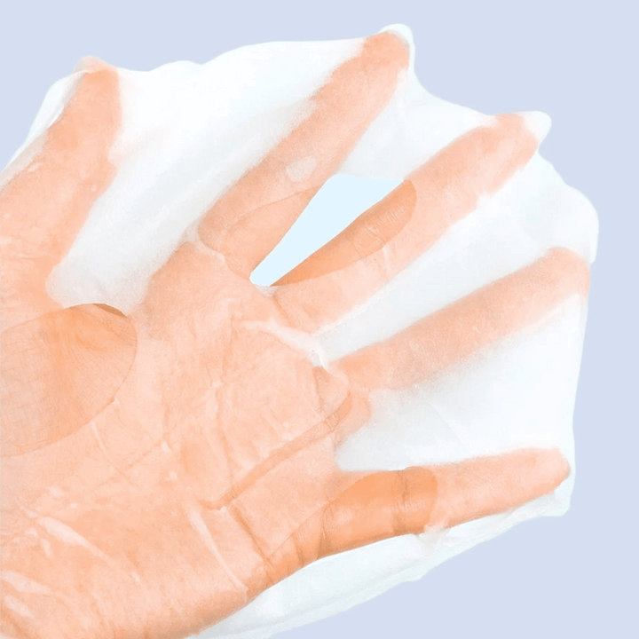 Priehľadná a vlhká pleťová maska je držaná na ruke proti svetlomodrému pozadiu. Maska je navrhnutá tak, aby pokrývala tvár s otvormi pre oči a ústa.