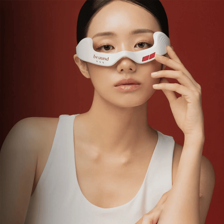 Fotografia modelu, na ktorej osoba používa Beaund Eye Rejuv, futuristické LED zariadenie pre oblasť okolo očí, na elegantnom červenom pozadí.