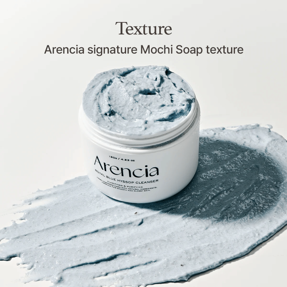 Otvorená nádoba s Arencia Fresh Blue Hyssop Rice Mochi Cleanser, umiestnená na rozotrenej vrstve modrej, krémovej čistiacej formulácie, ktorá ukazuje jej textúru podobnú mochi.