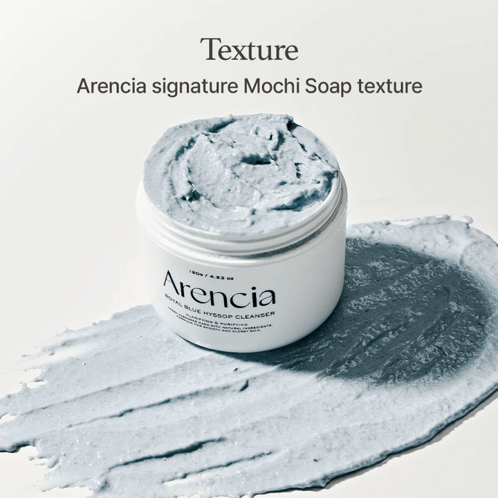 Otvorená nádoba s Arencia Fresh Blue Hyssop Rice Mochi Cleanser, umiestnená na rozotrenej vrstve modrej, krémovej čistiacej formulácie, ktorá ukazuje jej textúru podobnú mochi.