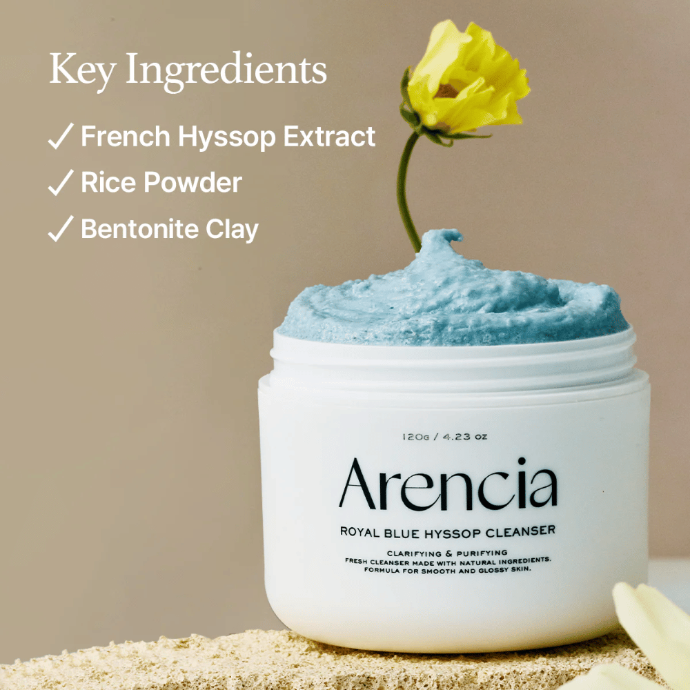 Obrázok nádoby "Arencia Royal Blue Hyssop Cleanser" naplnenej modrým čistiacim krémom. Zo smotany vyčnieva žltý kvet. Text na obrázku zdôrazňuje tri kľúčové zložky: výťažok z francúzskeho yzopu, ryžový prášok a bentonitový íl.