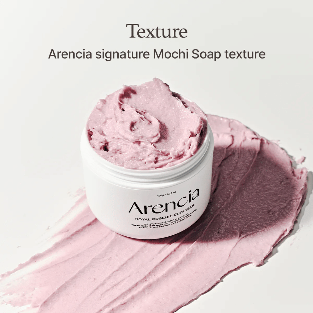 Nádoba s Arencia Royal Rosehip Cleanser je viditeľná na rozotretom ružovom čistiacom prostriedku s textúrou podobnou mochi. Text nad ňou opisuje produkt ako Arenciin podpis textúry.