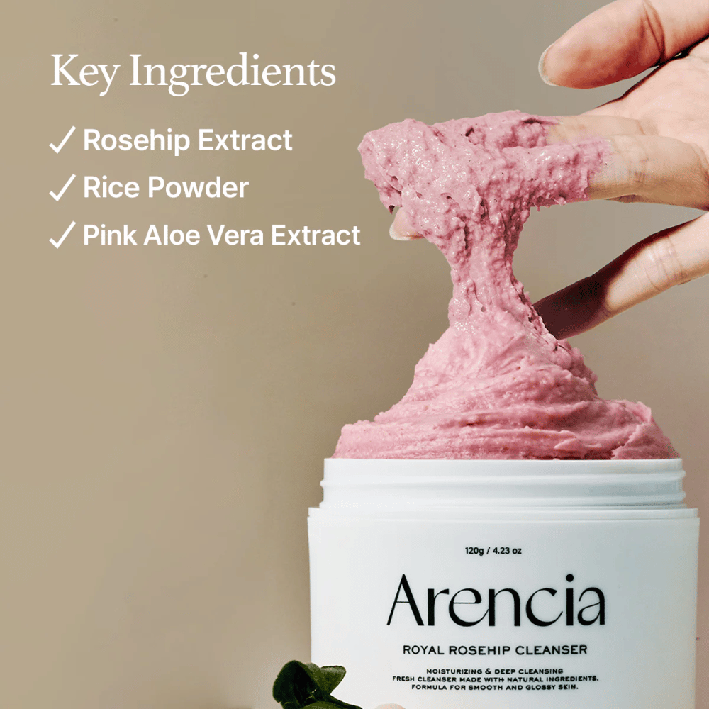 Ruka zdvíha ružovú, nadýchanú čistiacu textúru z nádoby Arencia Royal Rosehip Cleanser, s ingredienciami vľavo: extrakt zo šípok, ryžový prášok a extrakt z ružovej aloe vera.