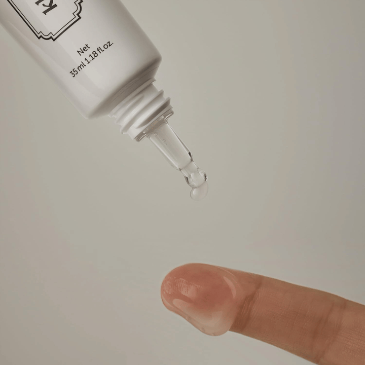 Detailný záber, na ktorom sa číry, ľahký gél nanáša z úzkeho hrotu na prst. Obrázok ilustruje transparentnú, gélovú konzistenciu produktu a presnú aplikáciu v okolí očí.