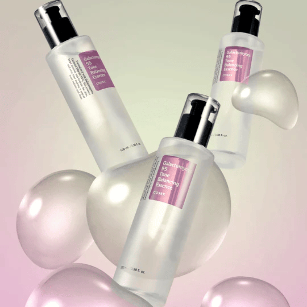 Tri fľaše COSRX Galactomyces 95 Tone Balancing Essence obklopené svetlými bublinkami. Esencia zlepšujúca pokožku, ktorá vyrovnáva tón pleti a dodáva prirodzený lesk.