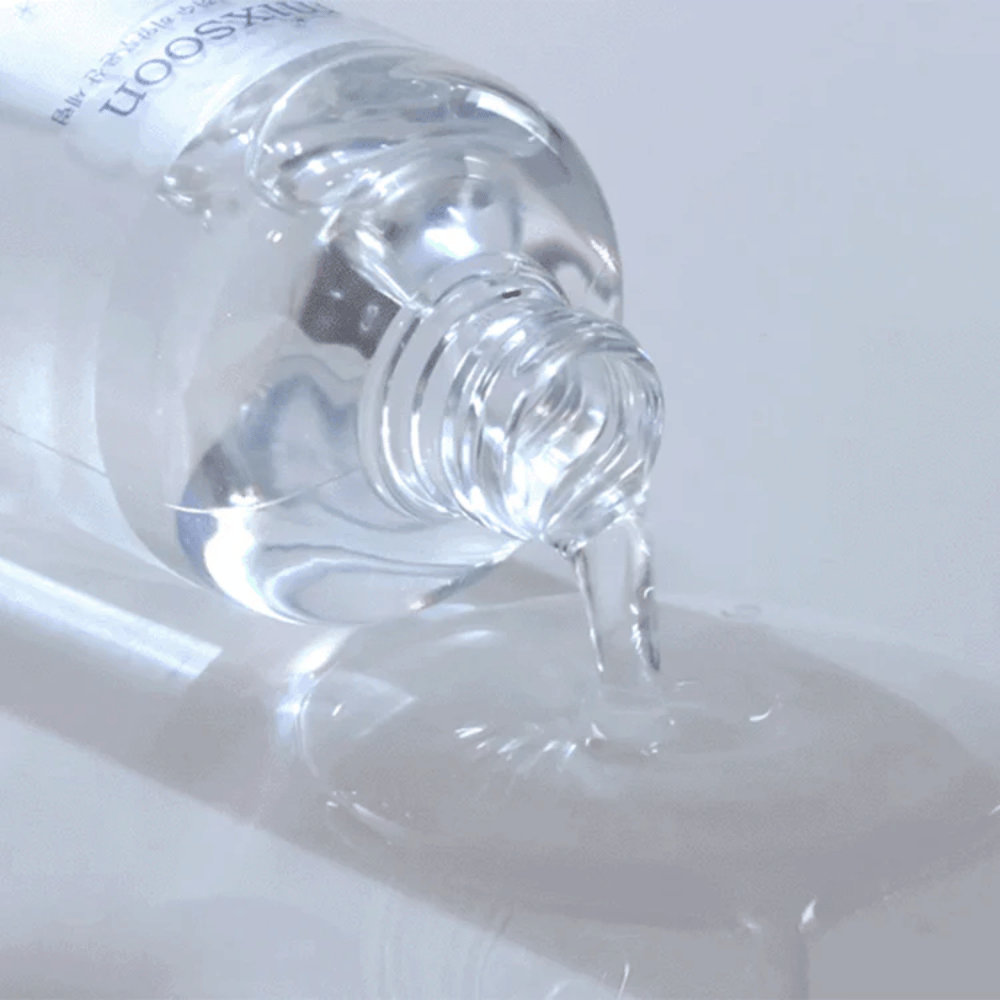 Detailný záber na priehľadné sérum, ktoré sa leje z fľaše Mixsoon Glacier Water Hyaluronic Acid Serum na lesklý povrch.