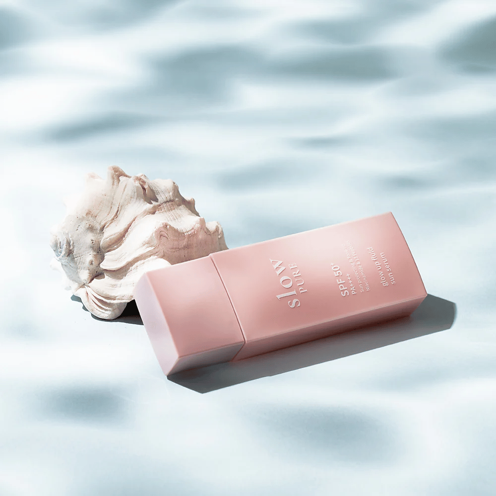 Slow Pure Glow Up Fluid Sun Serum pri mušliach a efektom vody, zvýrazňuje ochranu pred slnkom a lesk.