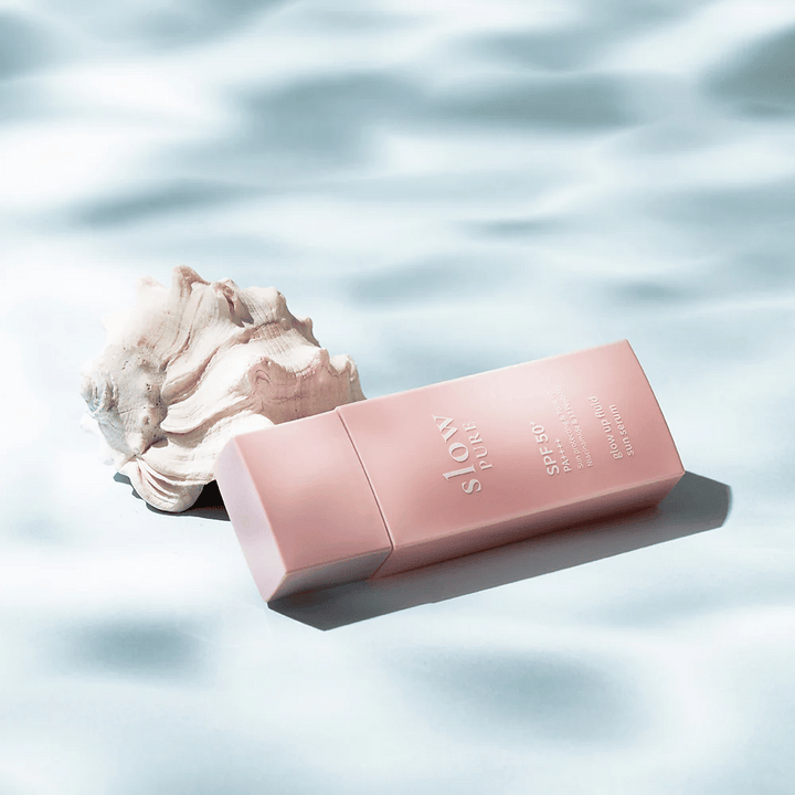 Slow Pure Glow Up Fluid Sun Serum pri mušliach a efektom vody, zvýrazňuje ochranu pred slnkom a lesk.