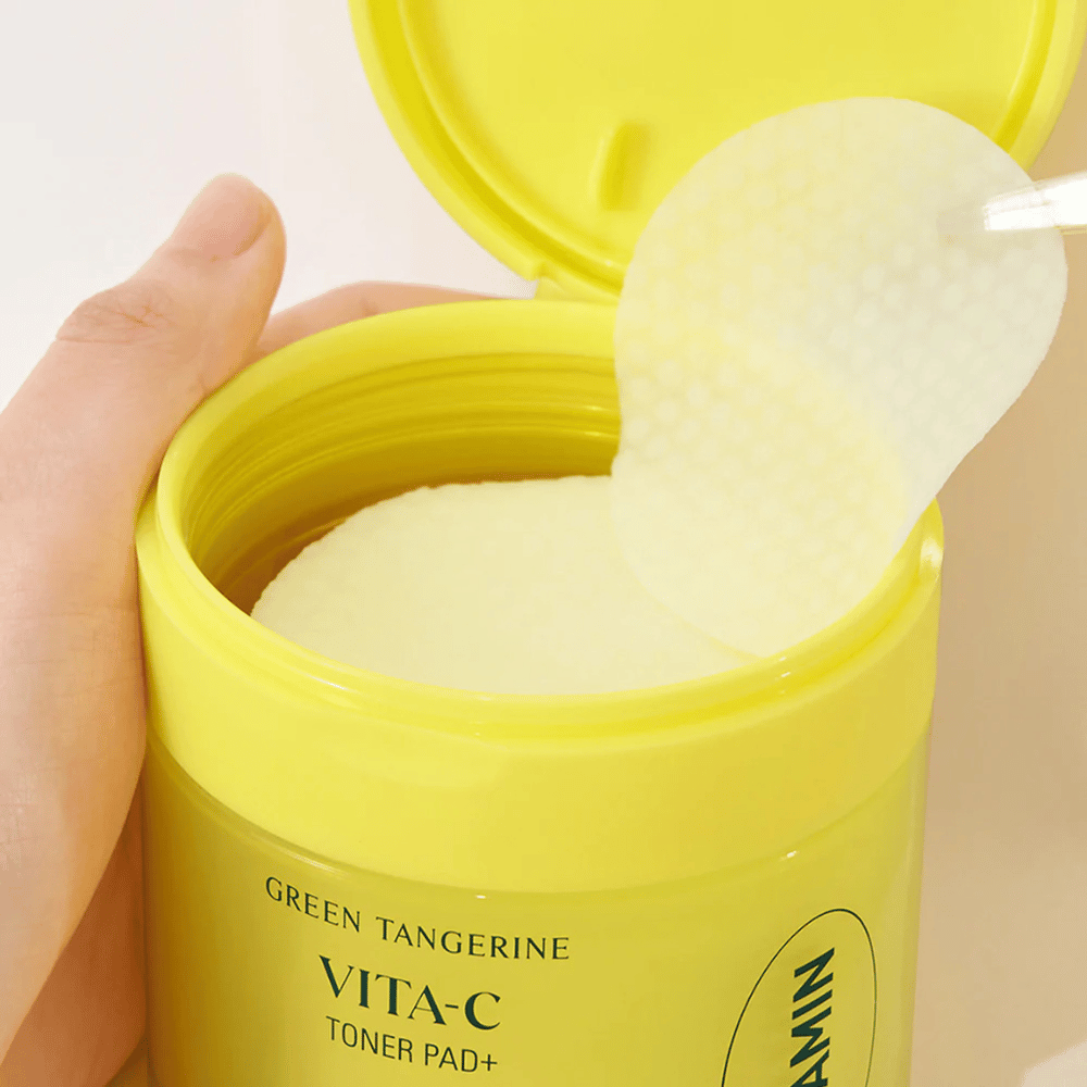 Ruka používa plastovú pinzetu na vybratie textúrovanej tonerovej podložky zo svetložltého obalu označeného "GREEN TANGERINE VITA-C TONER PAD+" značky "goodal".