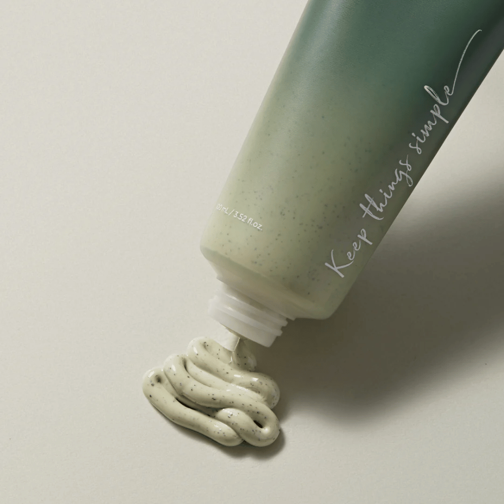 Zelená tuba s textom "Keep things simple" napísaným bielou farbou. Tuba leží na svetlom povrchu a zelenkastý produkt s malými čiernymi bodkami je vytláčaný. Vyzerá to ako maska na tvár alebo exfoliačný produkt. Na tube je uvedené 80 ml / 3.52 fl. oz.