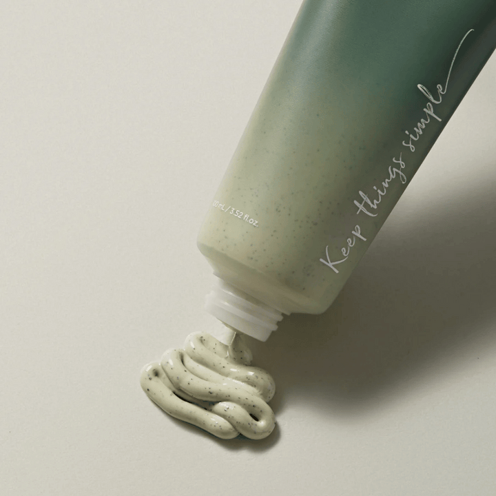 Zelená tuba s textom "Keep things simple" napísaným bielou farbou. Tuba leží na svetlom povrchu a zelenkastý produkt s malými čiernymi bodkami je vytláčaný. Vyzerá to ako maska na tvár alebo exfoliačný produkt. Na tube je uvedené 80 ml / 3.52 fl. oz.