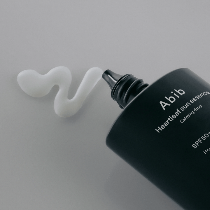 Detailný záber na Abib Heartleaf Sun Essence Calming Drop s opaľovacím krémom vytlačeným v bielej, vlnitej línii na svetlom povrchu.