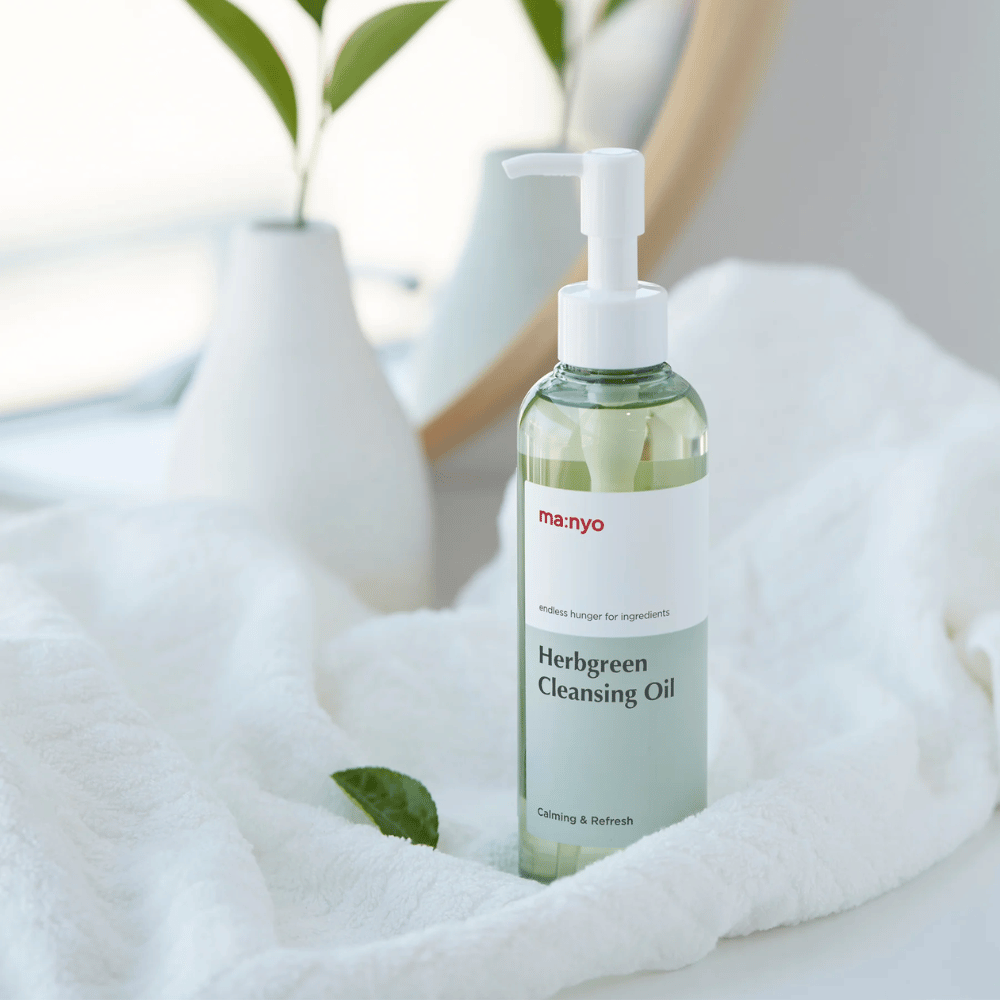 ma:nyo Herbgreen Cleansing Oil v pumpičkovej fľaši umiestnený na bielej uteráku, upokojujúci čistiaci olej s bylinnými zložkami pre jemné čistenie tváre
