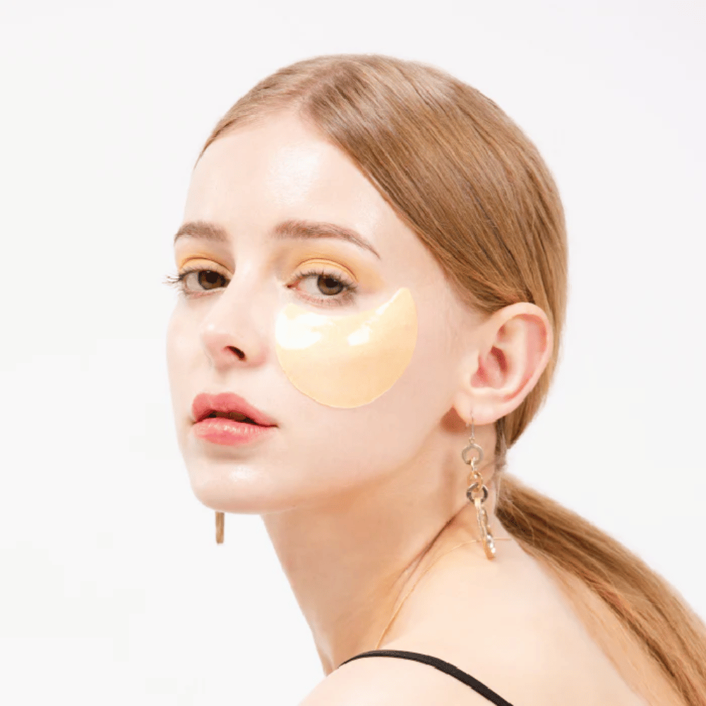 Modelka nosí zlaté trblietavé hydrogélové očné náplasti pod okom pre žiarivý efekt.