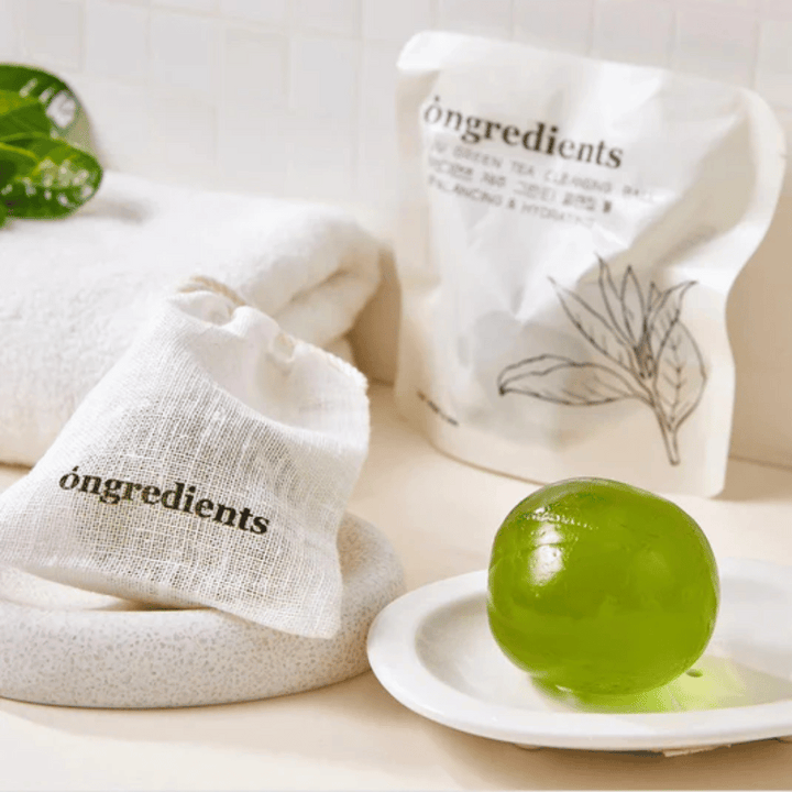 Óngredients Jeju Green Tea Cleansing Ball umiestnená na tanieri s balením a uterákom – jemné čistenie so zeleným čajom z Jeju.