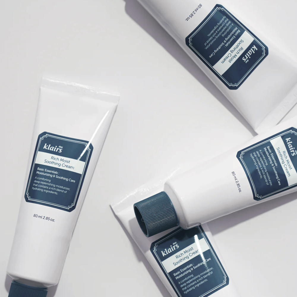 Viacero tub Klairs Rich Moist Soothing Cream strategicky umiestnených na svetlom povrchu, s tieňmi, ktoré vytvárajú hĺbku.