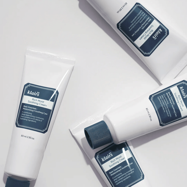 Viacero tub Klairs Rich Moist Soothing Cream strategicky umiestnených na svetlom povrchu, s tieňmi, ktoré vytvárajú hĺbku.