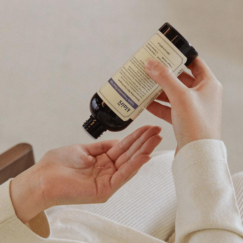 Osoba drží fľašu Klairs Supple Preparation Facial Toner hore nohami nad svojou rukou, pripravená dávkovať produkt.