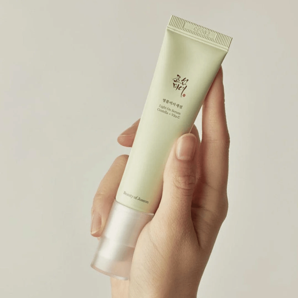 Ruka drží Beauty of Joseon Light On Serum s Centella a vitamínom C, v svetlozelenej tube s minimalistickým dizajnom na neutrálnej pozadí.