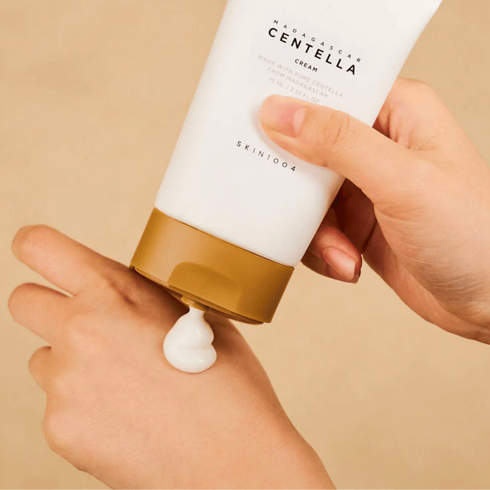 Obrázok zobrazuje osobu, ktorá drží tubu "Madagascar Centella Cream" od SKIN1004. Je to krém na pleť vyrobený z čistej Centelly z Madagaskaru, vo veľkosti 75 ml / 2.53 fl.oz. Krém sa aplikuje na ruku a je určený na výživu a hydratáciu pokožky.