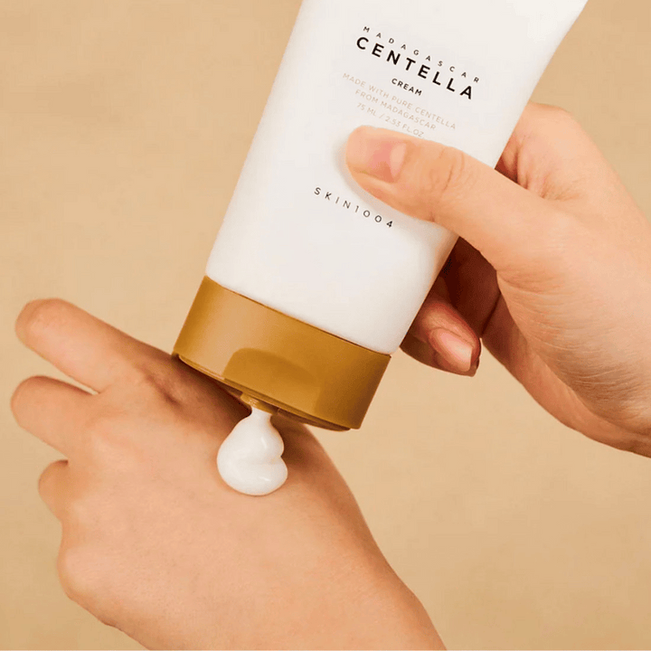 Obrázok zobrazuje osobu, ktorá drží tubu "Madagascar Centella Cream" od SKIN1004. Je to krém na pleť vyrobený z čistej Centelly z Madagaskaru, vo veľkosti 75 ml / 2.53 fl.oz. Krém sa aplikuje na ruku a je určený na výživu a hydratáciu pokožky.
