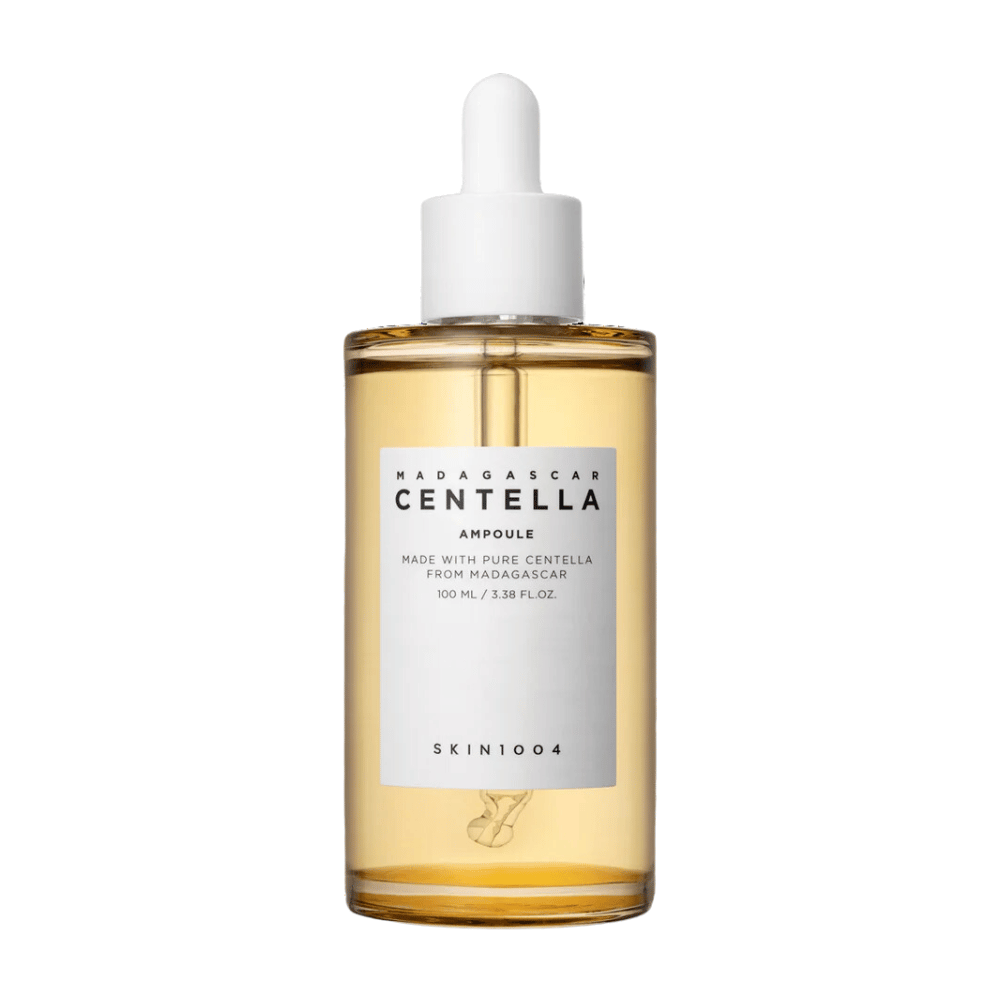 Obrázok ukazuje fľašu s "Madagascar Centella Asiatica 100 Ampoule" od SKIN1004. Fľaša obsahuje 100 ml a tvrdí, že je vyrobená z čistej centelly z Madagaskaru. Produkt vyzerá ako sérum na starostlivosť o pleť a jednoduchý štítok vytvára dojem čistoty a prirodzenosti. Fľaša s kvapkadlom naznačuje, že ide o starostlivo dávkovaný produkt na starostlivosť o pleť.