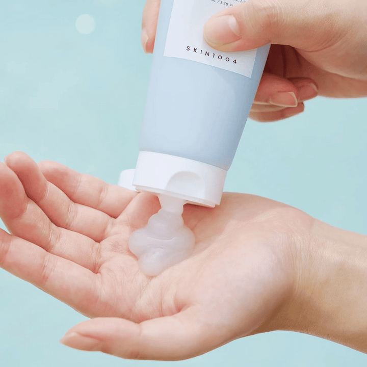 Obrázok zobrazuje niekoho, kto vytláča priehľadnú gélovú látku z tuby označenej "SKIN1004 Madagascar Centella Hyalu-Cica Sleeping Pack", ktorá obsahuje 100 ml produktu.