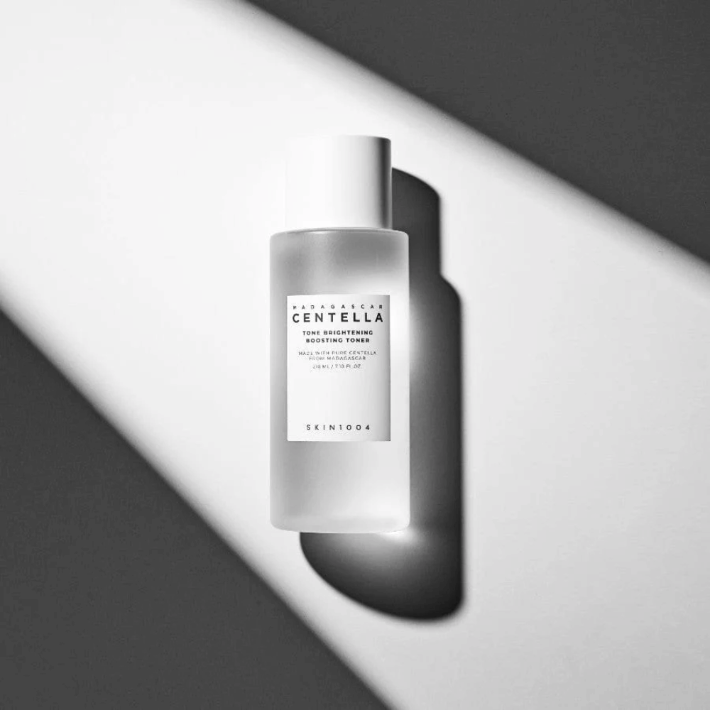 Fľaša SKIN1004 Madagascar Centella Tone Brightening Boosting Toner ležiaca na bielom povrchu s dramatickým tieňom v čiernobielom svetle.