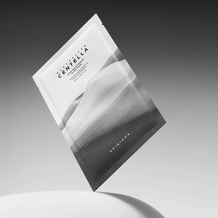 Balenie Sheet mask od SKIN1004 vznášajúce sa na sivom pozadí s minimalistickým dizajnom.