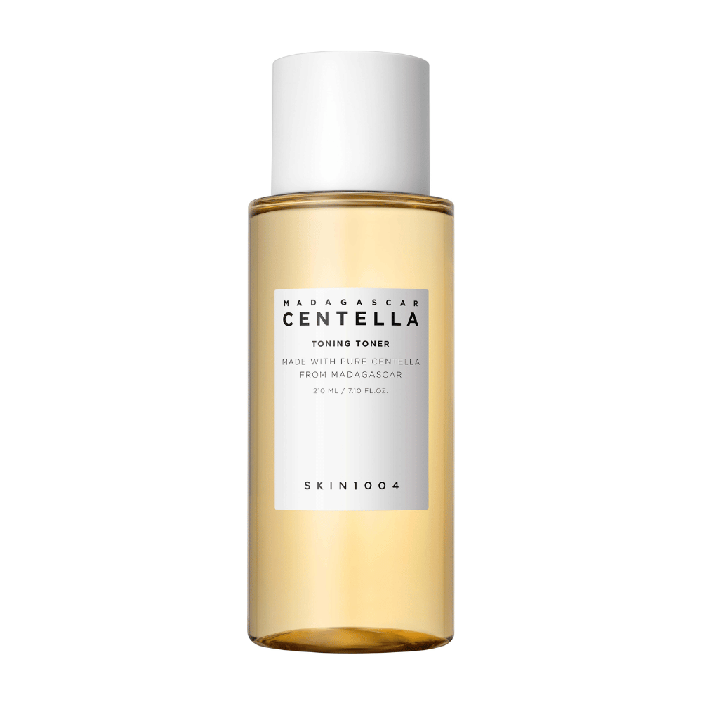 Obrázok zobrazuje fľašu s pleťovým tonerom, označenú ako "Madagascar Centella Toning Toner" od SKIN1004. Produkt je uvedený ako obsahujúci 210 ml alebo 7,10 fl.oz a je vyrobený s čistou Centellou z Madagaskaru. Balenie je jednoduché a elegantné s priehľadnou fľašou a zlatistou tekutinou vo vnútri, čo vytvára pocit luxusu a čistoty. Logo značky SKIN1004 je jasne viditeľné v dolnej časti etikety.